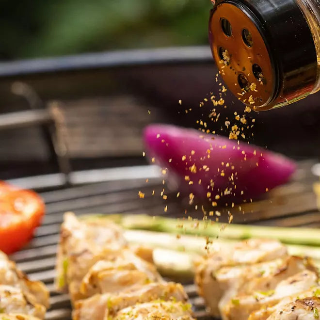 Sprinkling Montreal Chicken seasoning over grilled chicken and vegetables

